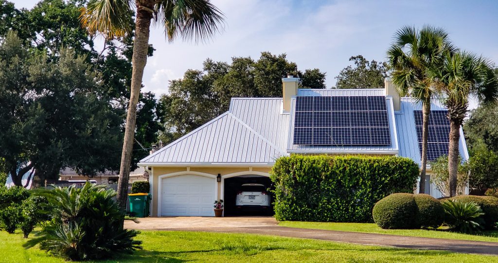 Home with beach vibes has solar panels on rooftop surrounded by tropical palm trees.